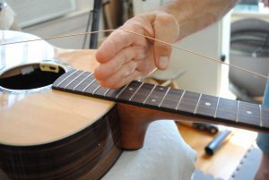 Figure 5. With four fingers of one hand under the string at either the 14th fret or where the neck meets the body, pull the string taut.