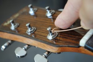 Figure 8. Fold the excess string back over on itself as shown above. Once the fold has been made, keep it pinned with your index finger and begin turning tuner to wind the string on the tuning peg so the string is on the inside of the tuner.